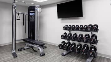 Academia com barra para puxar, banco de musculação e suporte com halteres.