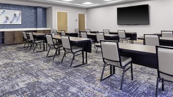 Un salón de conferencias con varias mesas y sillas, una pantalla grande y suelo alfombrado.