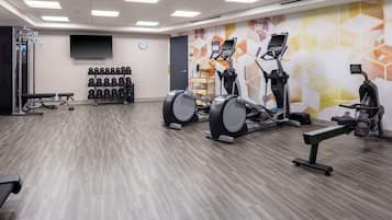 Een sportschool met cardioapparaten, gewichtrekken en een televisie aan de muur.
