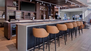 Een moderne bar met een lange toonbank, barstoelen en diverse flessen en glazen.
