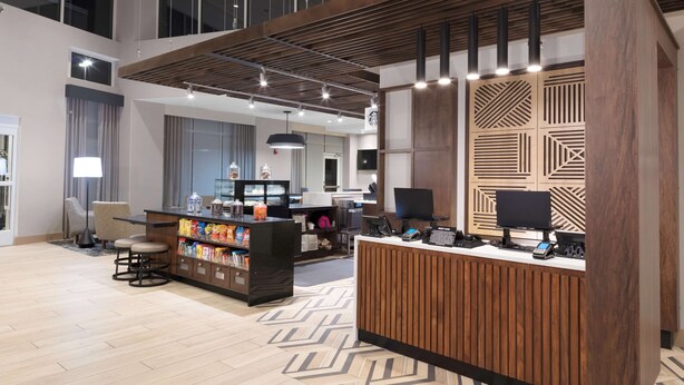 Een moderne hotel lobby met een receptiebalie, een zithoek en een groot raam.
