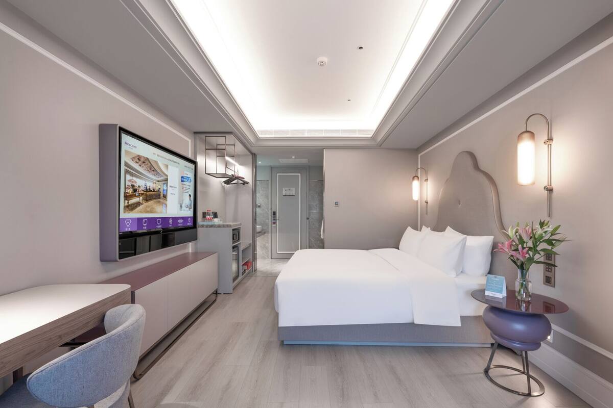 Een moderne hotelkamer met een bed, bureau, stoel en een televisie waarop een uitzicht van de kamer te zien is.
