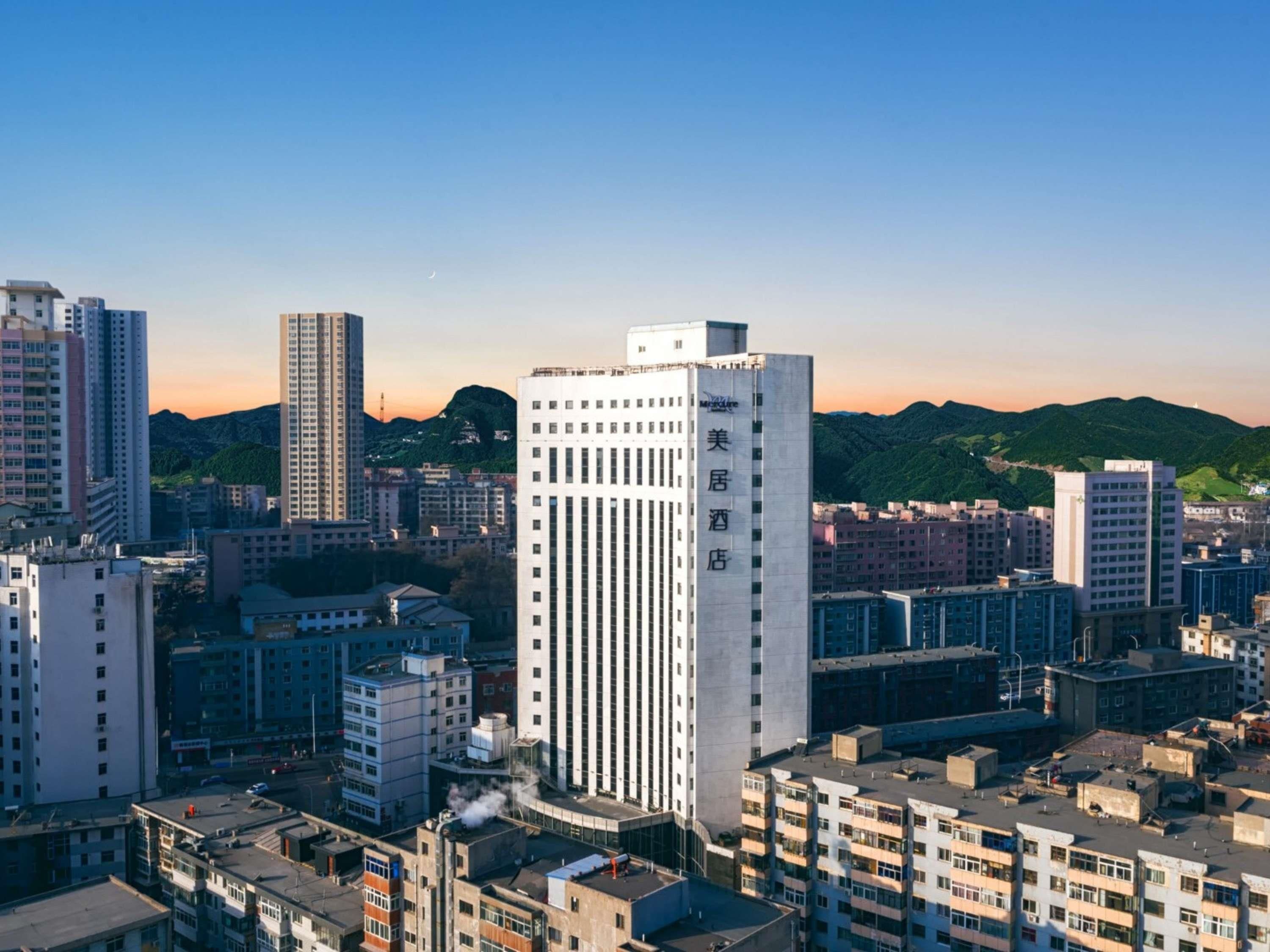 A high-rise hotel with multiple floors, surrounded by other buildings and a mountainous backdrop.