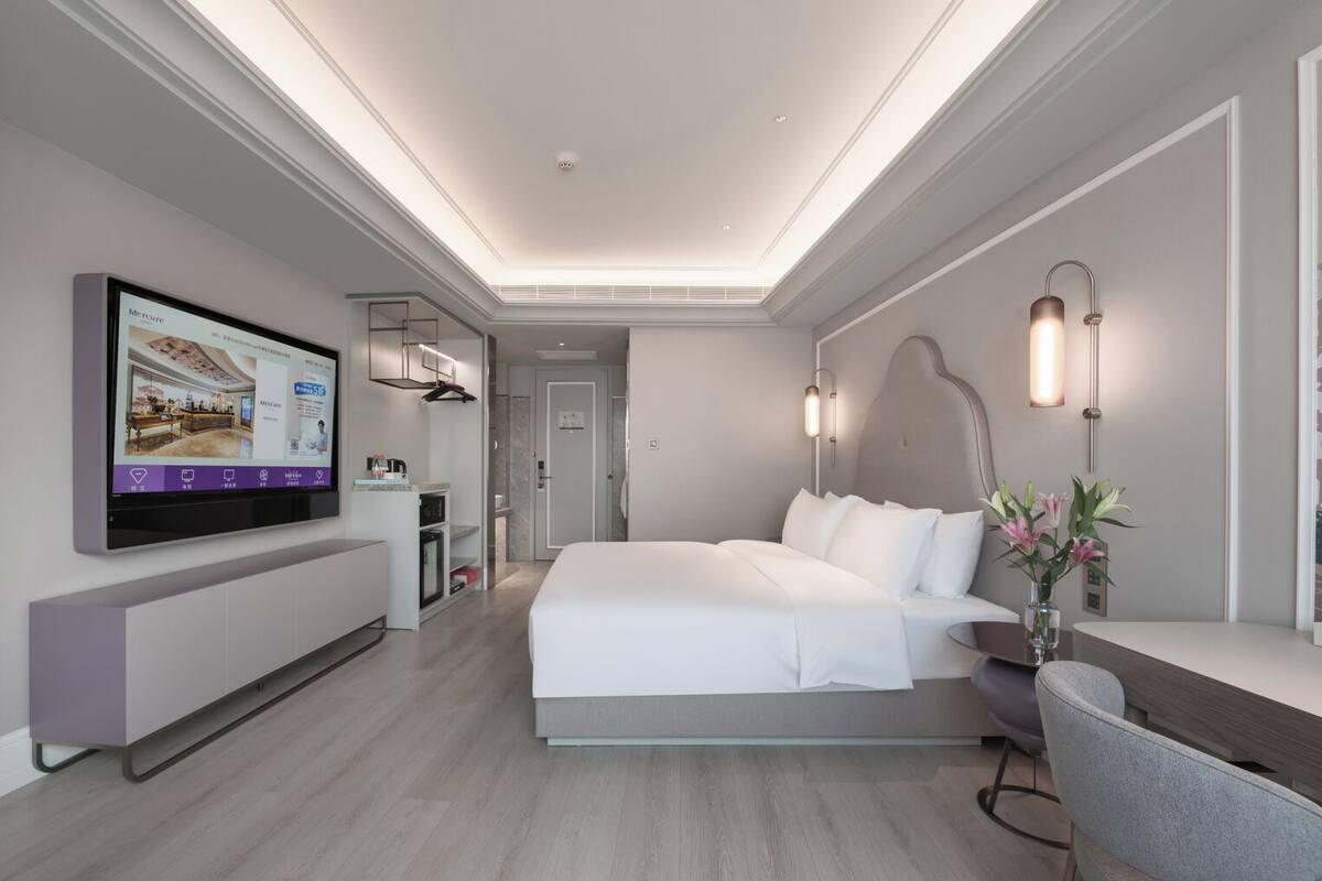 Een moderne hotelkamer met een groot bed, een bureau, een aan de muur bevestigde televisie en een zichtbare badkamer door een geopende deur.
