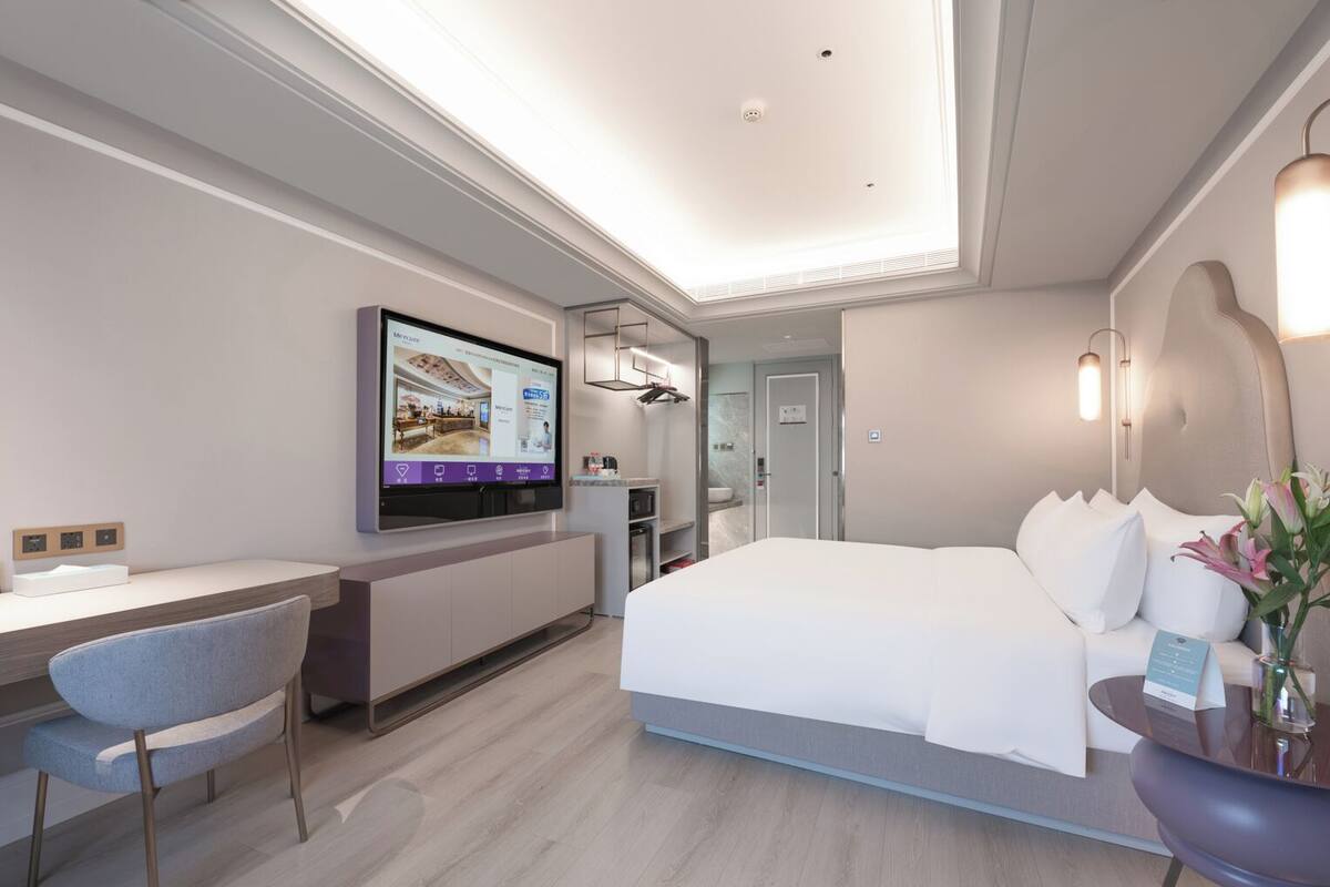 Een moderne hotelkamer met een bed, bureau, stoel, televisie en een zichtbare badkamer door een open deur.