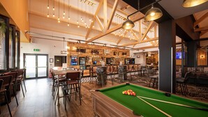 A bar area with wooden beams, hanging lights, and a pool table.