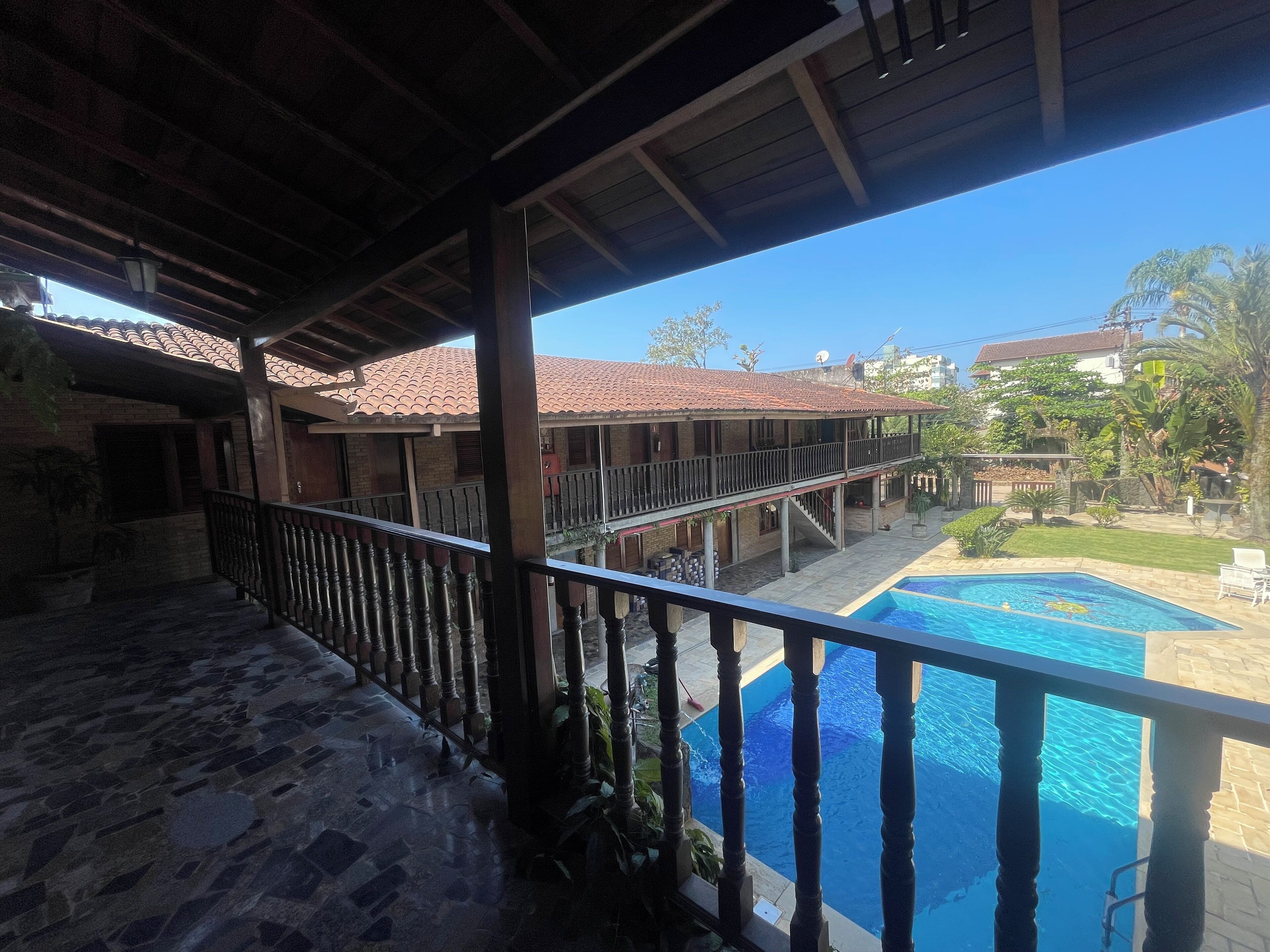 A covered outdoor area with a pool, stone flooring, and a view of a residential building with a tiled roof.