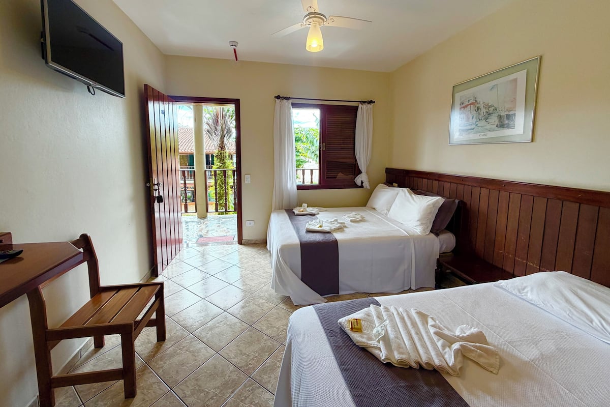 A hotel room with two beds, a desk, a TV, a ceiling fan, and a balcony.