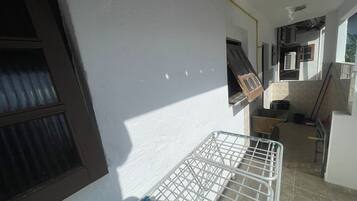A narrow corridor with a metal laundry basket, a window with blinds, and a door leading to a kitchen area.