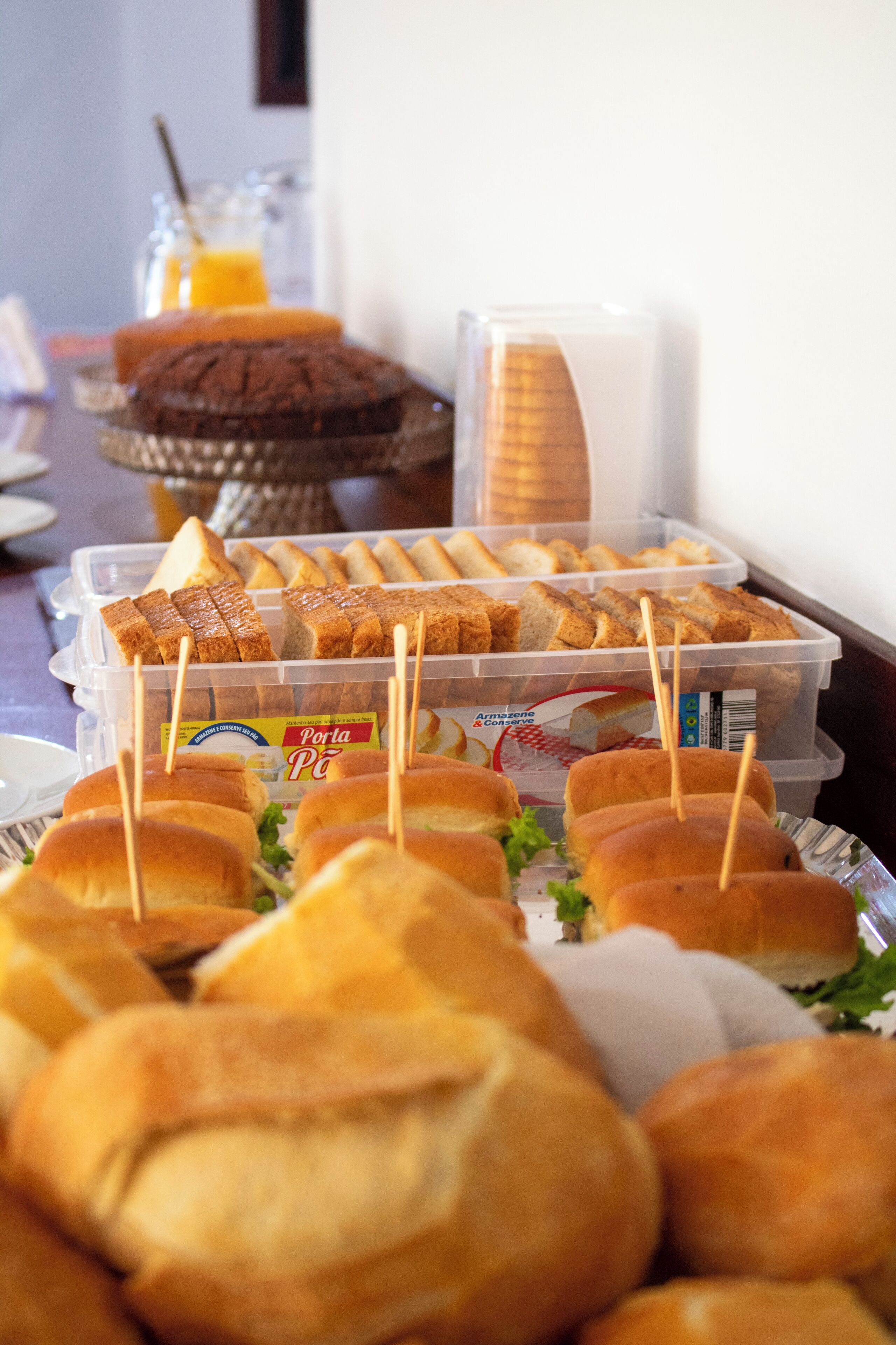 A buffet table with various food items including sandwiches, bread, and a juice dispenser.