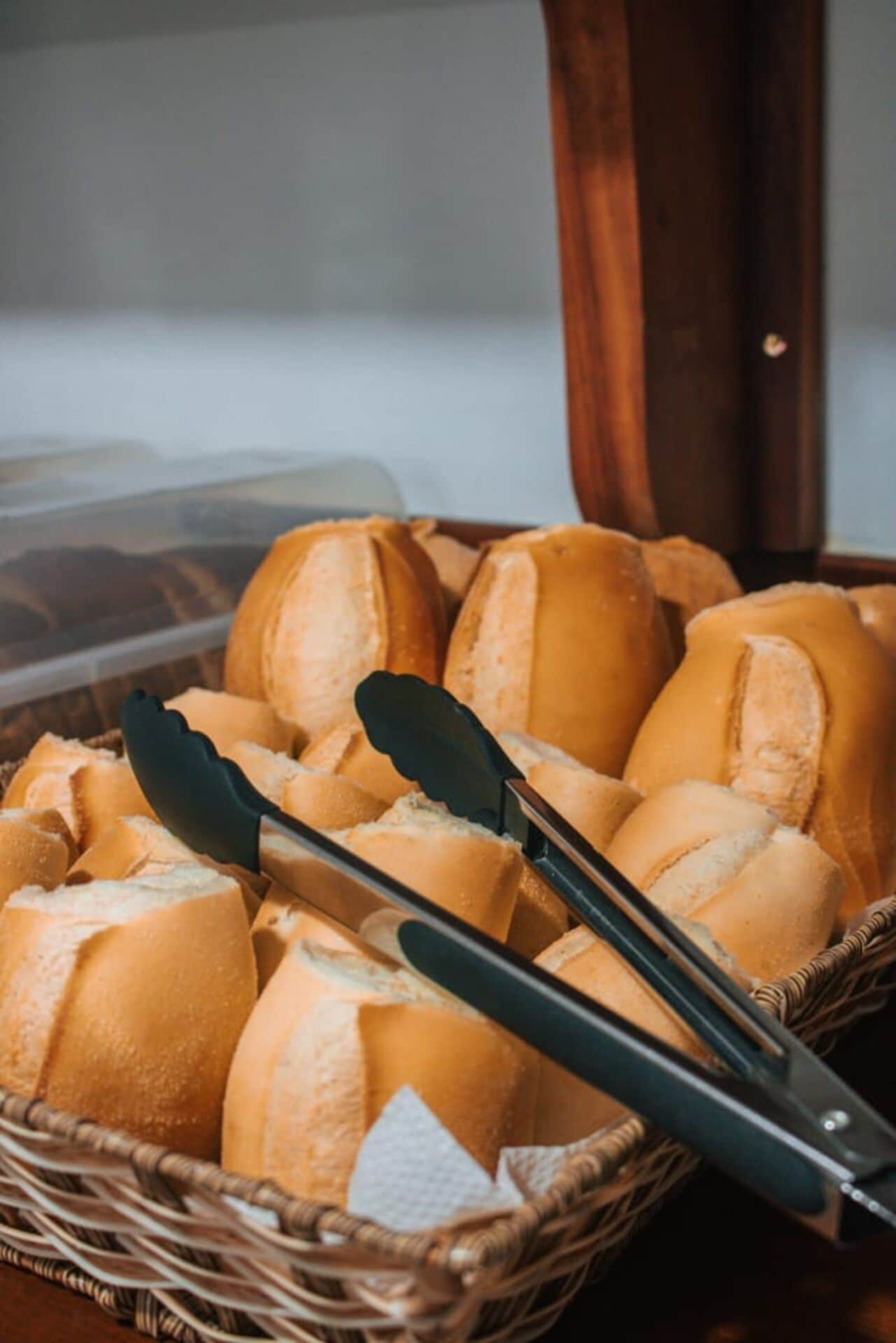 A basket of baguettes with a pair of tongs on top.