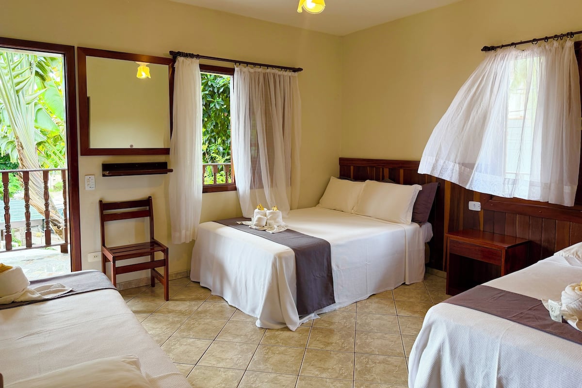 A hotel room with a bed, a chair, a small table, a window with curtains, and a ceiling fan.
