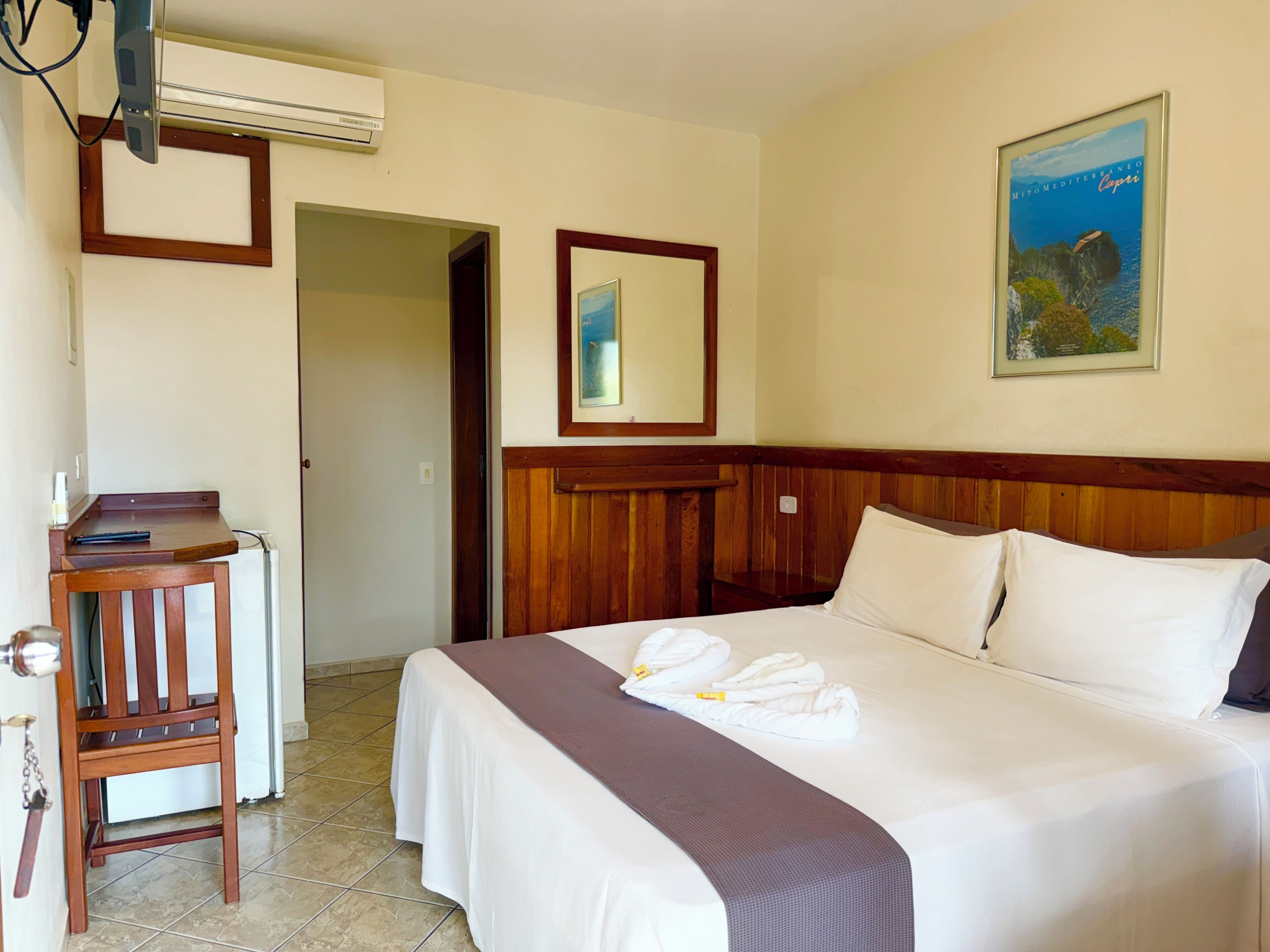 Ein Hotelzimmer mit Bett, Schreibtisch, Stuhl, Spiegel und einem gerahmten Bild an der Wand.