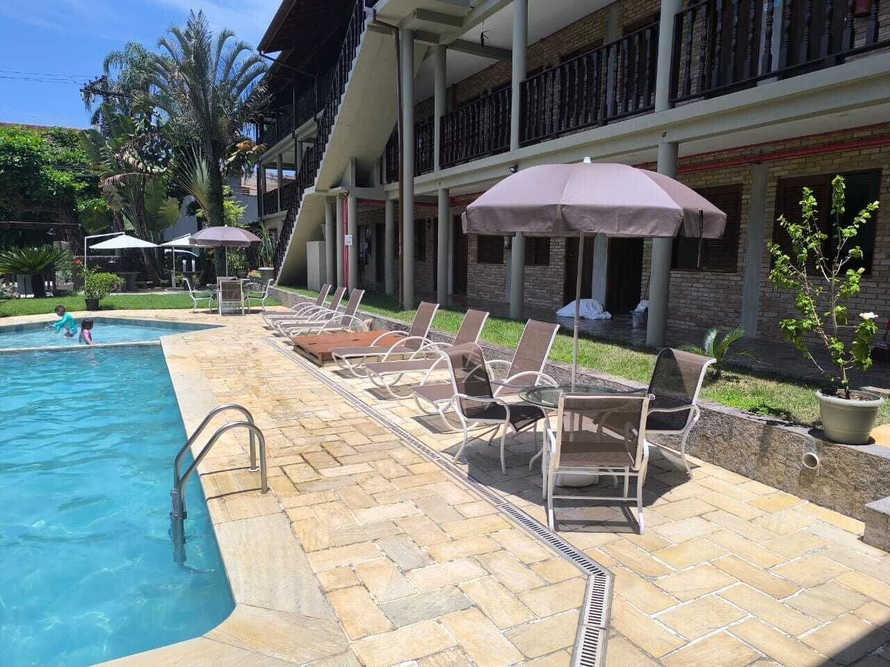 A pool area with lounge chairs and umbrellas, a staircase leading to a balcony, and a brick building with a balcony.