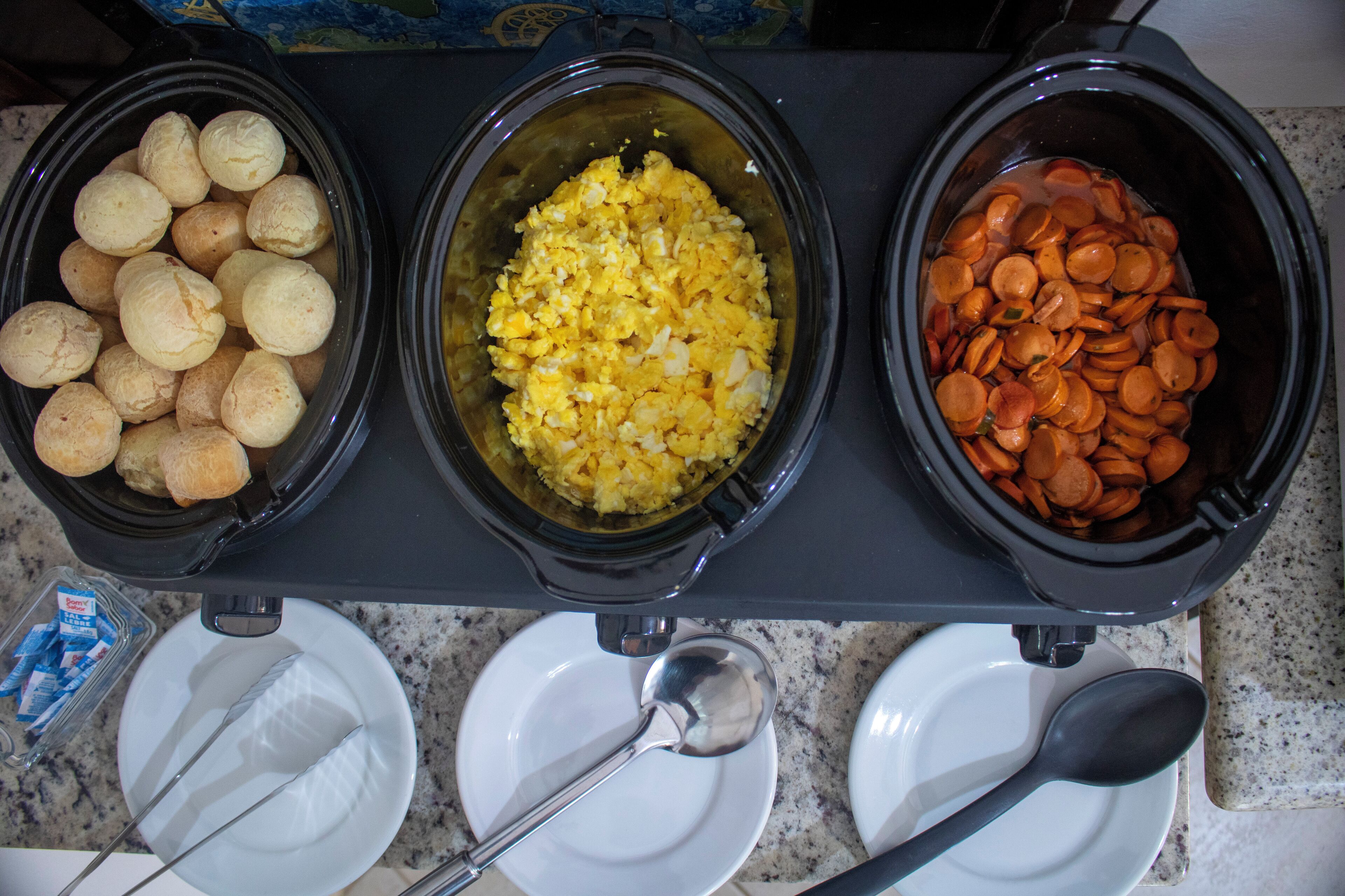 Tres platos para olla de cocción lenta en una encimera: uno con panecillos, uno con huevos revueltos y uno con zanahorias en rodajas.