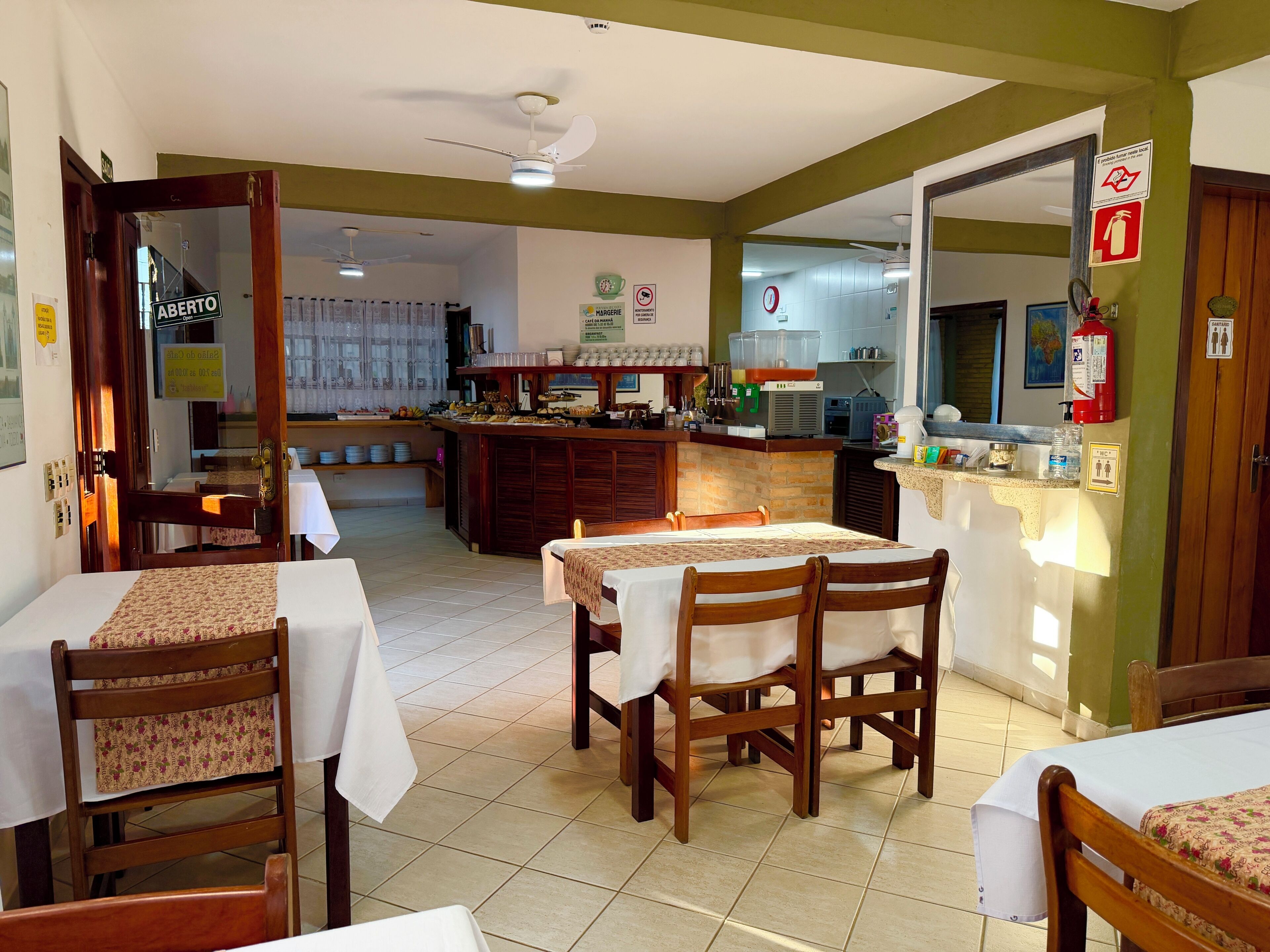 A hotel dining area with tables, chairs, a bar, and a kitchen in the background.