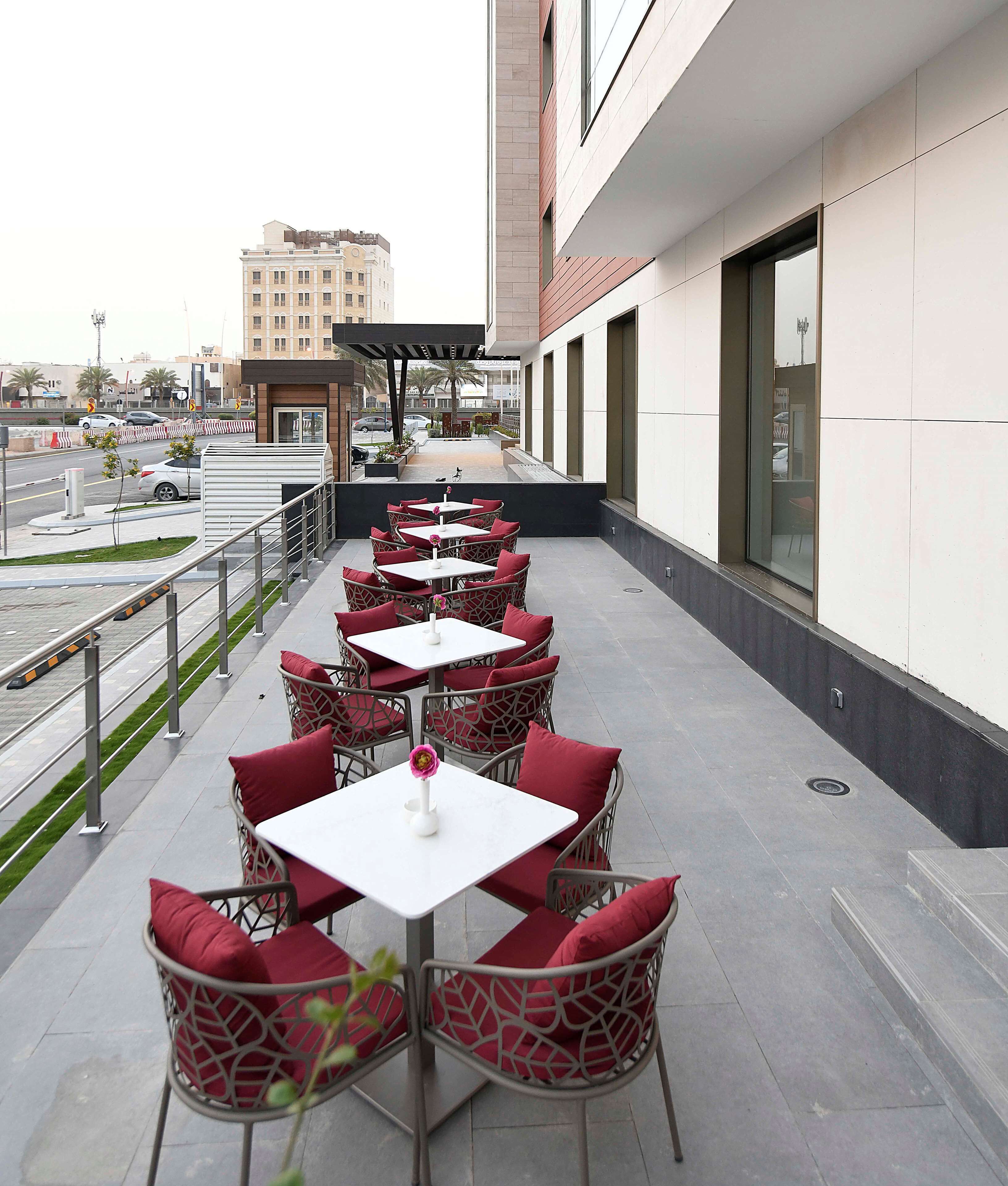 An outdoor patio with multiple tables and chairs, a view of the street, and a building in the background.