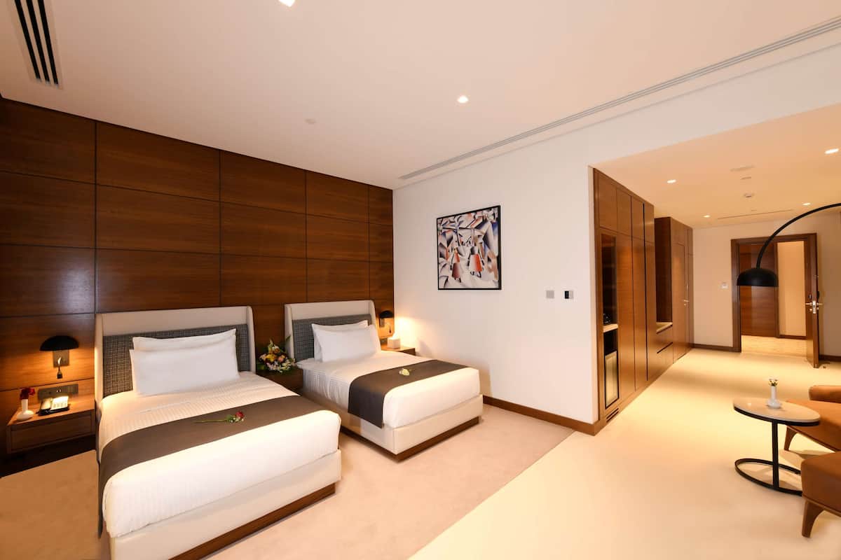 A modern hotel room with two beds, a small table, and a seating area.