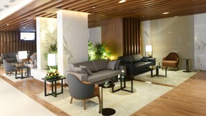 A modern lobby with a grey sofa, armchairs, and a coffee table. There are plants and a small table with a lamp. - Golden Tulip Riyadh (Riyadh)
