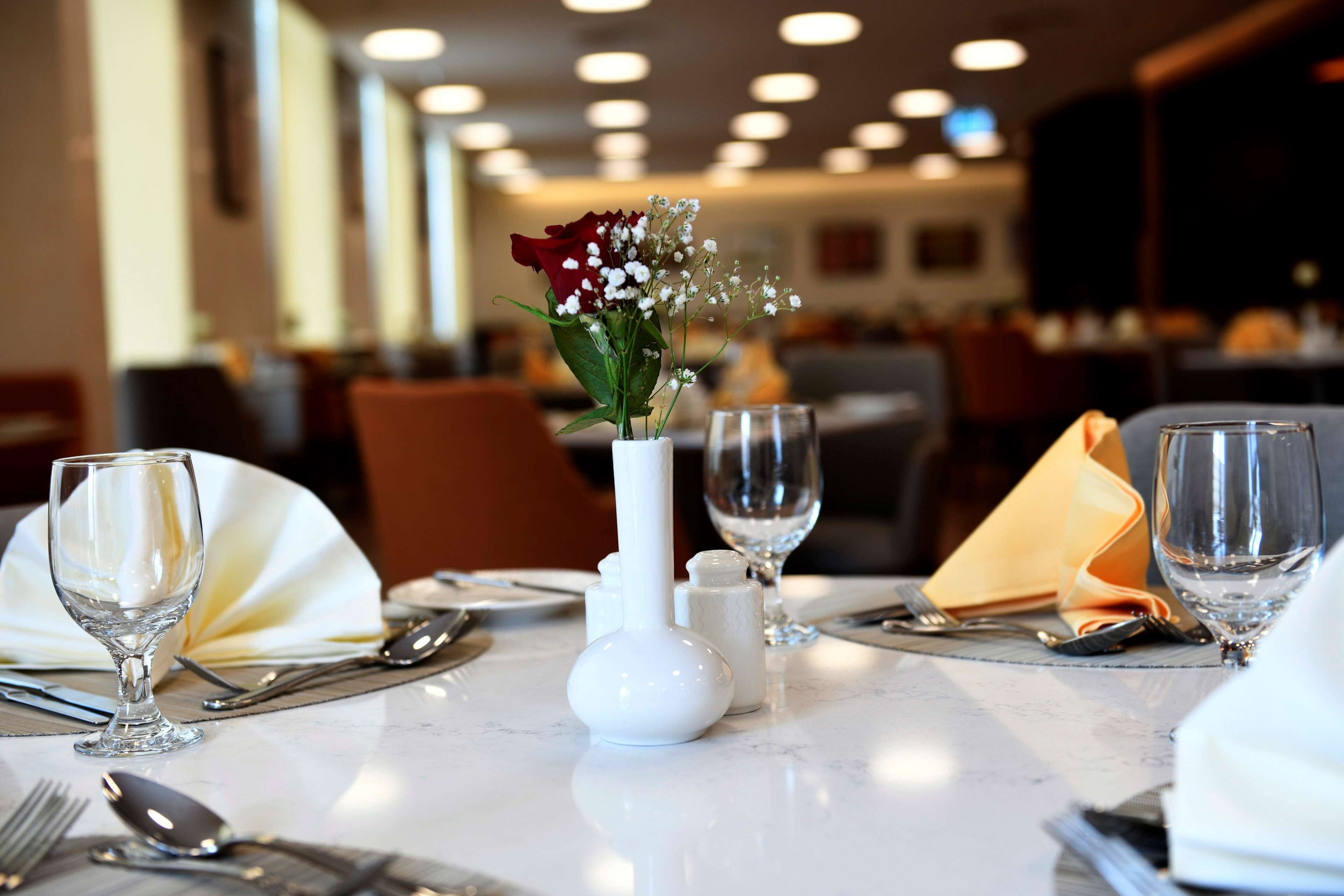 A dining table set with white tableware, a vase with flowers, and salt and pepper shakers.