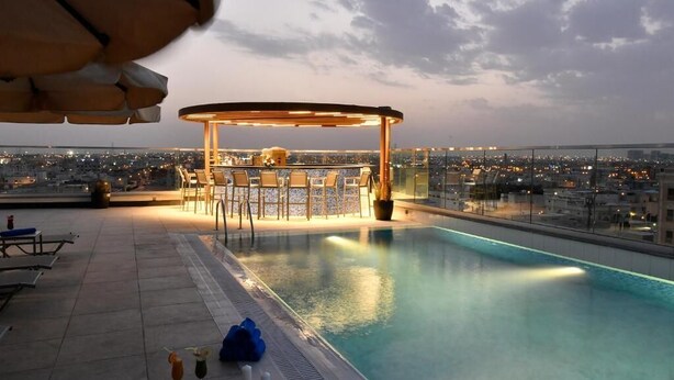 A rooftop pool area with a bar and lounge chairs, overlooking a cityscape at dusk. - Golden Tulip Riyadh (Riyadh)