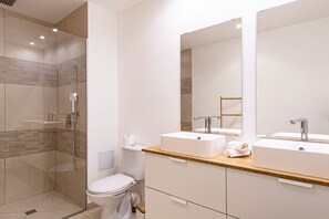 A modern bathroom with a glass shower enclosure, two sinks, and a large mirror. - Orient Bay Beach Front Apartment (Collectivity of Saint Martin)