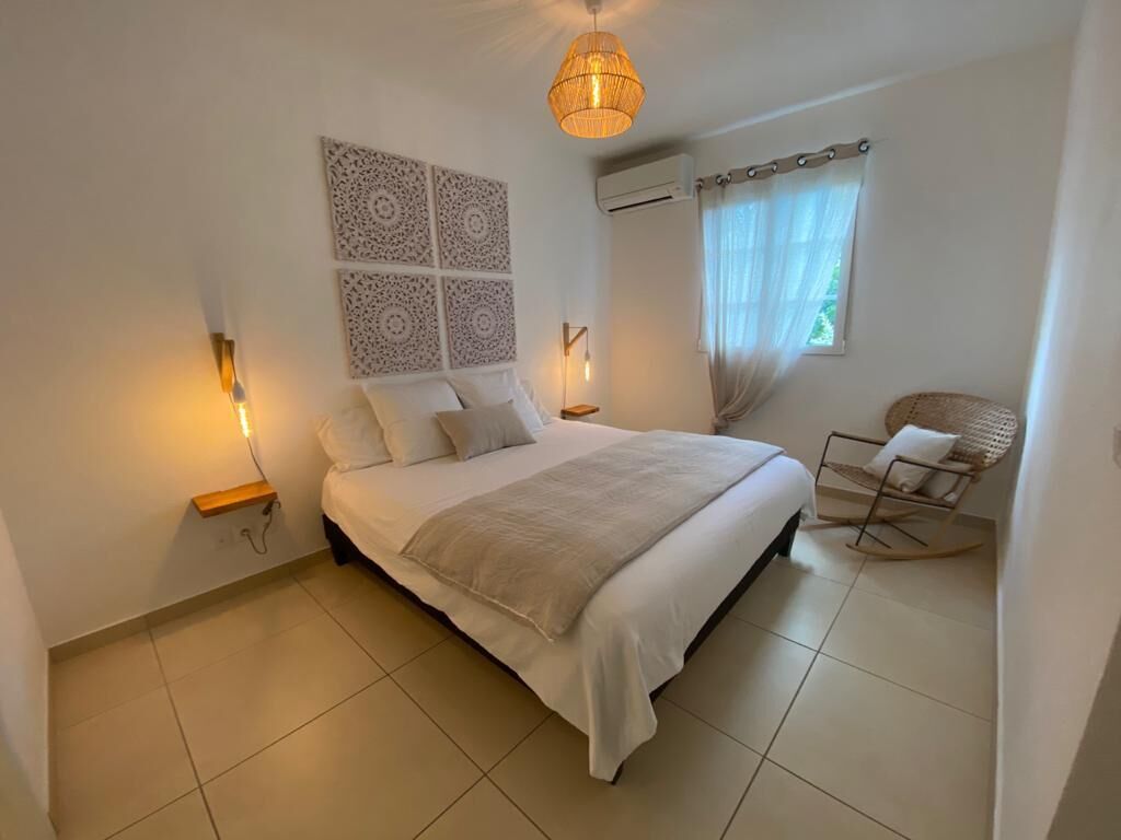 Une chambre avec un grand lit, un climatiseur fixé au mur, un luminaire au plafond et une fenêtre avec des rideaux.