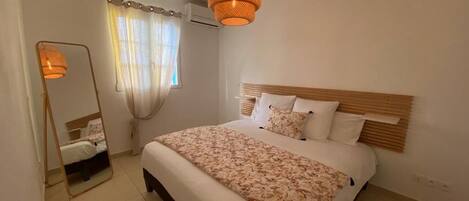 A bedroom with a bed, a mirror, and a hanging light fixture.