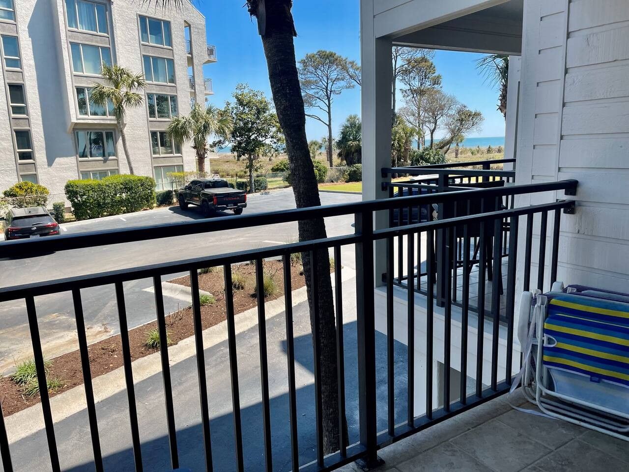 A balcony with a metal railing overlooking a street with parked cars and a building in the background.