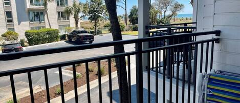 A balcony with a metal railing overlooking a street with parked cars and a building in the background.