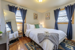 Une chambre bien rangée, avec un lit, une table de chevet, un miroir et une fenêtre avec des rideaux.