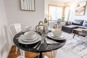 A dining area with a round table set for four, white chairs, and a black marble table. There is a sofa and a coffee table in the background. - Stylish & Spacious Royal Oak Getaway! (Royal Oak)