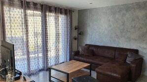 Een moderne woonkamer met een houten salontafel, een bruine leren bank en een televisie op een houten dressoir.