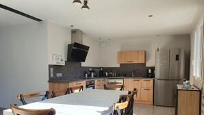 Een moderne keuken met een centraal eiland, houten keukenkastjes, roestvrijstalen apparatuur en een eethoek met een witte tafel en houten stoelen.