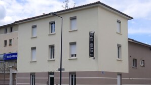 Een meerlaags gebouw met een beige gevel, meerdere ramen en een bord waarop staat dat het een hotel is.