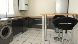 Een kleine keuken met een wasmachine, een koelkast en een barkruk.