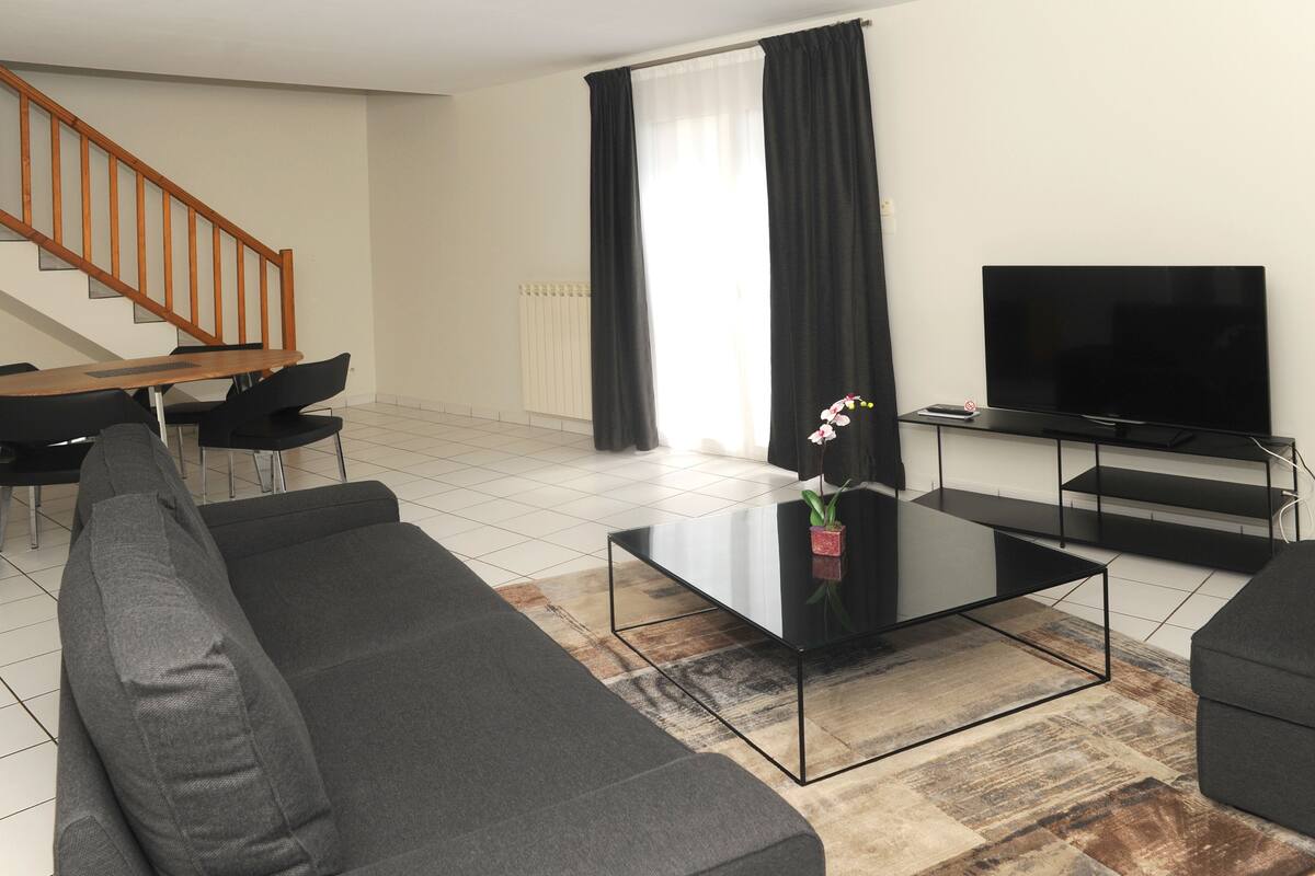 A modern living room with a sofa, coffee table, TV, and a staircase.
