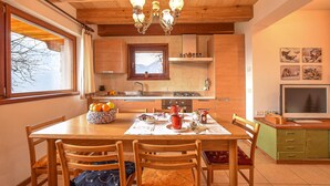 A cozy kitchen with wooden cabinets, a dining table with chairs, a chandelier, and a television. - Cozy home in Telve di Sopra (Telve di Sopra)