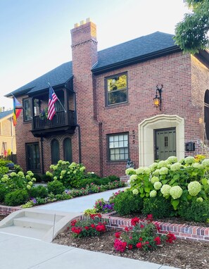 A brick house with a balcony, a front door, and a well-maintained garden with various plants and flowers. - Old World Charm Basement Level Flat in upscale Cherry Creek (Denver)