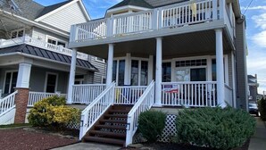 A two-story house with a balcony, a front porch, and a staircase leading to the entrance. - 2 min walk to boardwalk, beach or town from this 2nd floor 4br 2ba gem! (Ocean City)