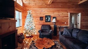 Ein gemütliches Blockhaus-Interieur mit Holzbalkendecke, Weihnachtsbaum, Ledersofa, Couchtisch und Kamin.