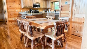 Ein rustikales Holzinterieur mit einem Esstisch und Stühlen aus Baumstämmen, einer Küche mit Holzausstattung und einem Holzboden.