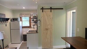 A compact kitchen with a refrigerator, microwave, and a sliding wooden door leading to another room. - Sunny Cottage at Cozy Nook (Lake George)