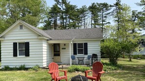 A white house with black shutters, a porch, and two red Adirondack chairs. - Sunny Cottage at Cozy Nook (Lake George)