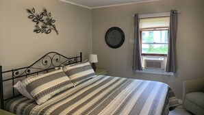 A bedroom with a bed, a wall clock, and a window with curtains. - Sunny Cottage at Cozy Nook (Lake George)