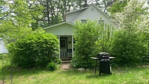 A small, single-story house with a green exterior and a front porch. - Hens & Chickens Cottage at Cozy Nook (Lake George)