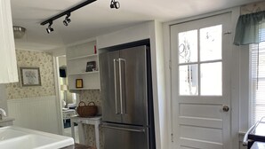 A kitchen with a stainless steel refrigerator, a white door with a window, and a wooden countertop. - Hens & Chickens Cottage at Cozy Nook (Lake George)
