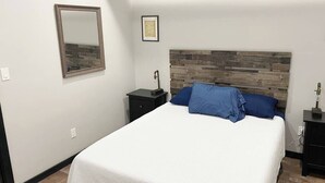 A bedroom with a bed, a nightstand, a mirror, and a headboard with a wooden panel design.
