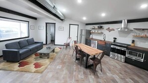 A modern kitchen with a dining area, a sofa, and a large window.