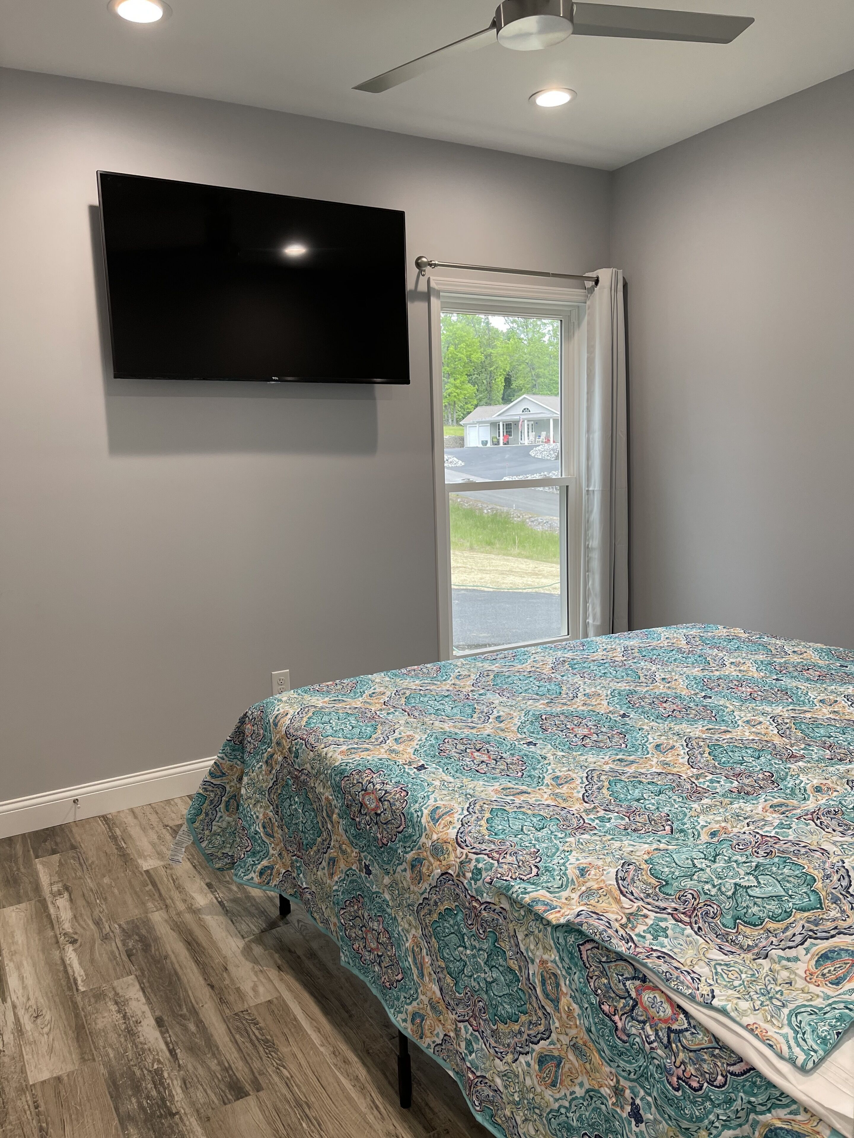 A bedroom with a bed, a flat-screen TV mounted on the wall, and a view of the outside through a glass door.